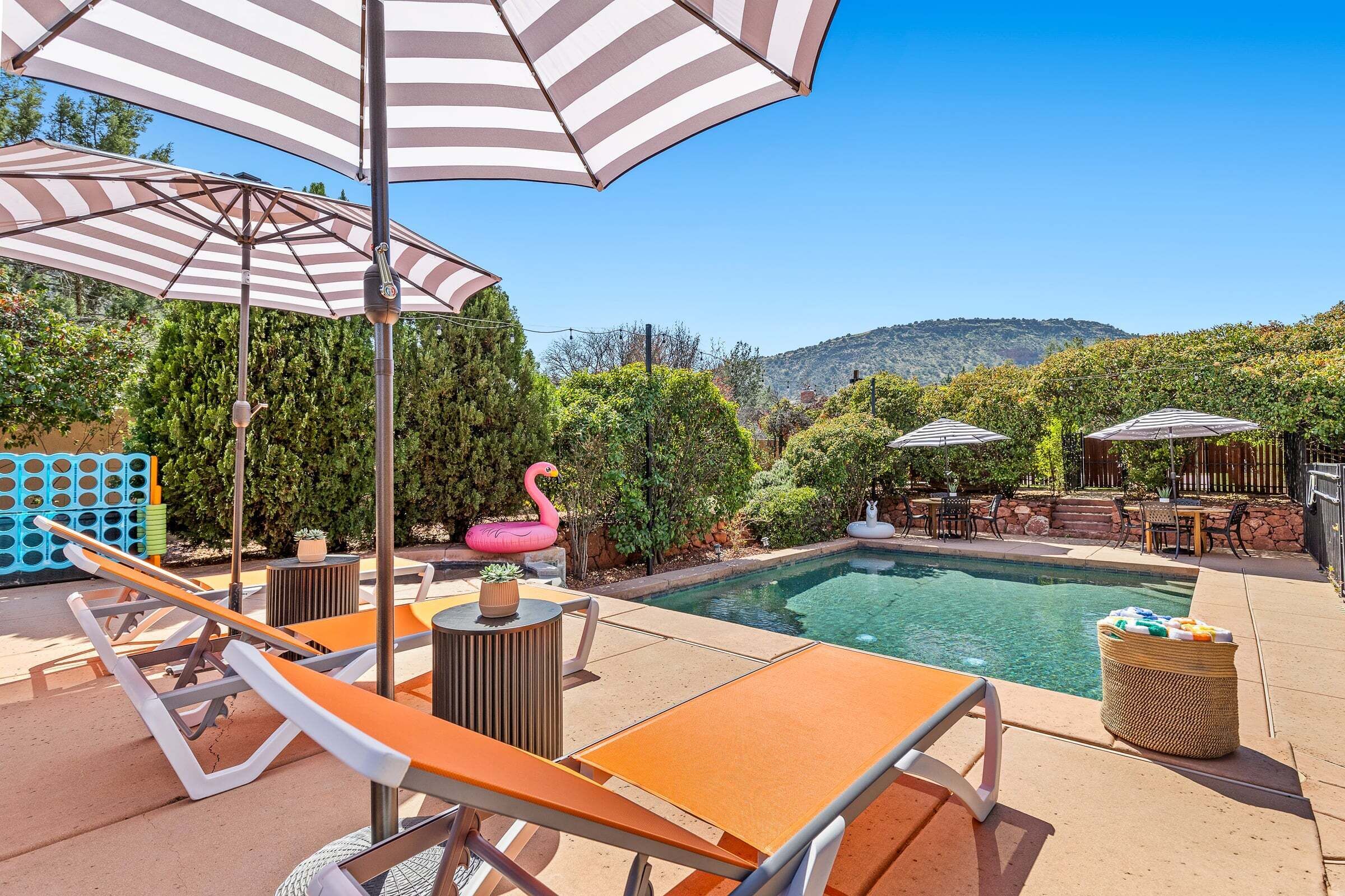 A poolside area with lounge chairs, striped umbrellas, and a flamingo float.