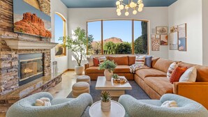 Ein Wohnzimmer mit Kamin aus Stein, einem großen Fenster, einer Couch und einem Couchtisch.