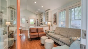 A spacious living area with a sofa, ottomans, and a dining table. A kitchen with cabinets and a microwave is visible in the background. - 5 min. Walk to Town & Beach, Greenbelt Views + Private Backyard (Pacific Beach)