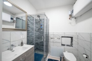 A modern bathroom with a glass-enclosed shower, a white sink, and a toilet.