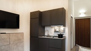 Een kleine keuken met een inbouwfornuis, een spoelbak en een flatscreen-tv boven de toonbank.