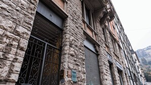 Een historisch gebouw van natuursteen, met een metalen hekwerk en luiken voor de ramen.