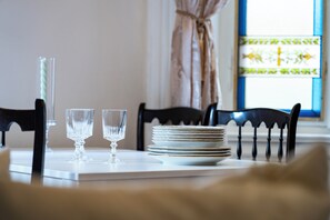 A dining table set with plates and glasses, chairs, and a window with curtains.