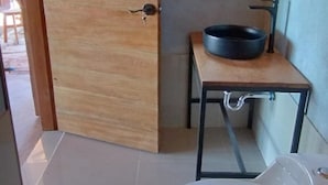 A small bathroom with a white toilet, a wooden door, a small window, and a black basin on a wooden table. - Casa de Primo (Capachica)