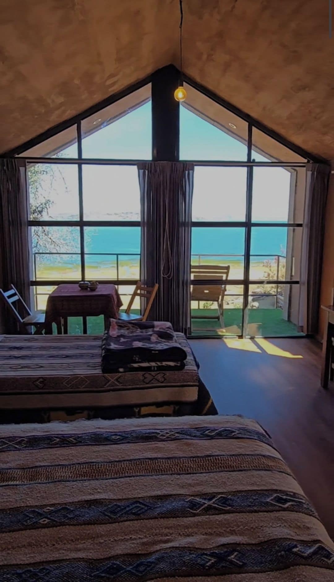 Un dormitorio con un ventanal grande, una cama, una mesa y una silla.