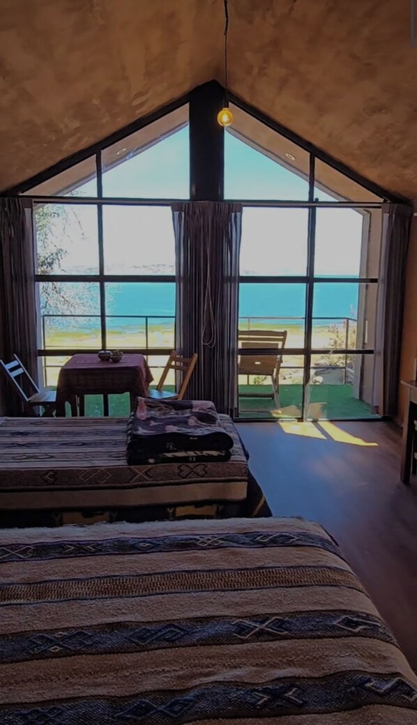 A bedroom with a large window, a bed, a table, and a chair. - Casa de Primo (Capachica)