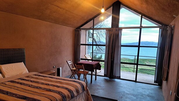 Un dormitorio con una cama grande, un escritorio y vistas al exterior a través de amplios ventanales.