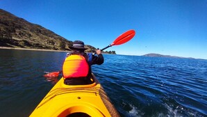 Una persona haciendo kayak en aguas tranquilas, bajo un cielo despejado y con tierra visible a lo lejos.