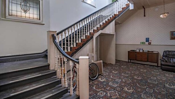 Una escalera con barandilla de madera y peldaños negros que conducen a una plataforma.