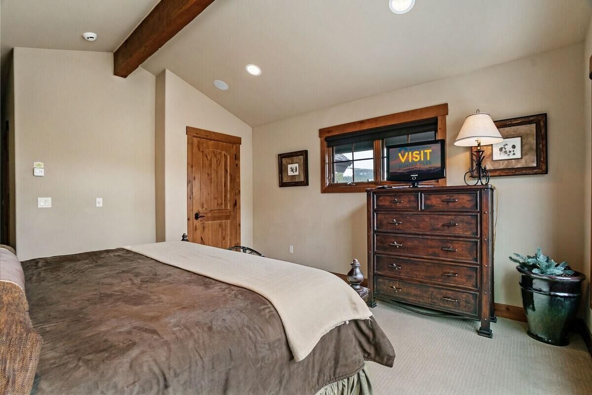 A bedroom with a bed, wooden dresser, a 'VISIT' sign, and a lamp.