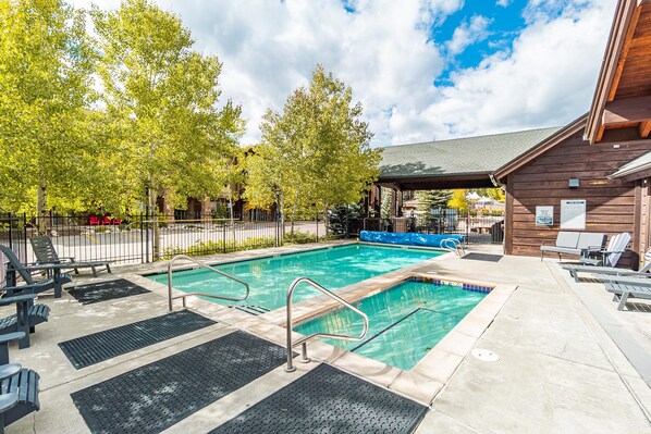 A swimming pool with a wooden deck, lounge chairs, and a covered area.