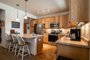 A modern kitchen with wooden cabinets, stainless steel appliances, and a bar area with stools.