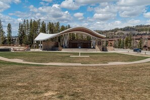 A large open pavilion with a curved roof, surrounded by a grassy area and a stone wall.