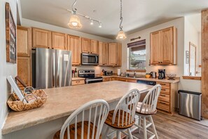 A modern kitchen with wooden cabinets, stainless steel appliances, a large island with bar stools, and pendant lighting.