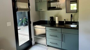 A compact kitchen with a sliding door leading to a balcony, built-in cabinets, a countertop with a coffee maker, and a mirror above the sink. - Modern Cozy Pebble Beach Studio with Premium Amenities and WiFi (Del Monte Forest)