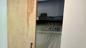 A room with a sliding wooden door, a closet with hanging clothes, a small trash bin, and a floor vent. - Modern Cozy Pebble Beach Studio with Premium Amenities and WiFi (Del Monte Forest)