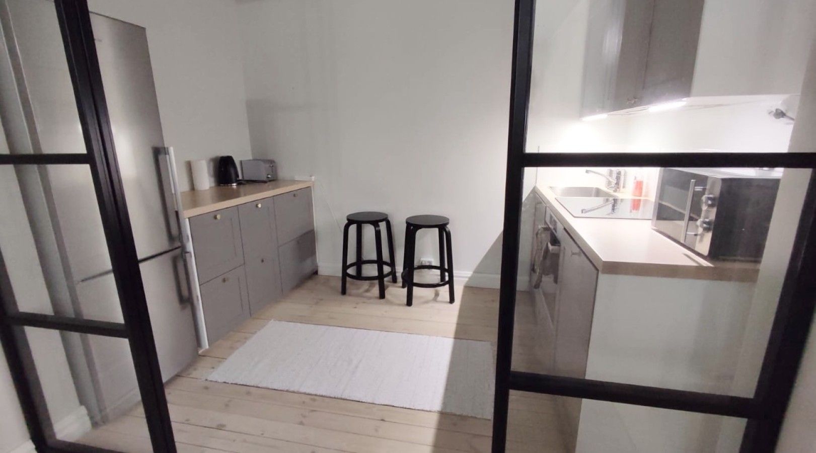 Una cocina compacta con un refrigerador, un lavamanos y dos taburetes.