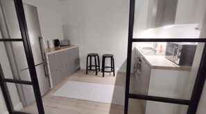 A compact kitchen with a refrigerator, a sink, and two stools.