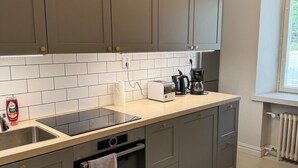 Une cuisine moderne avec des meubles gris, un plan de travail blanc, un four encastré et une fenêtre équipée de stores.