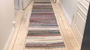 Un couloir avec un tapis rayé aux couleurs vives, des portes blanches et un plancher en bois.