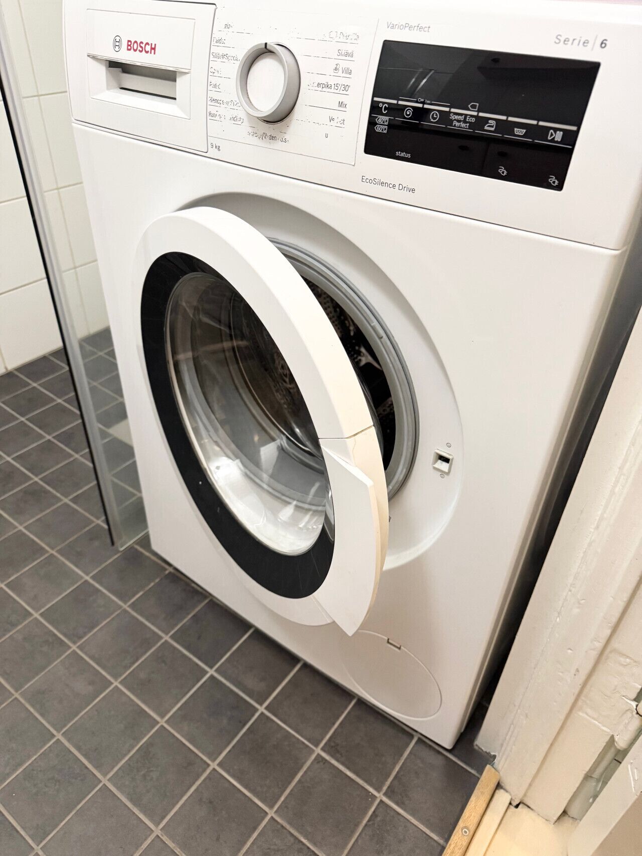A Bosch washing machine with a control panel, a front-loading door, and a tiled floor.