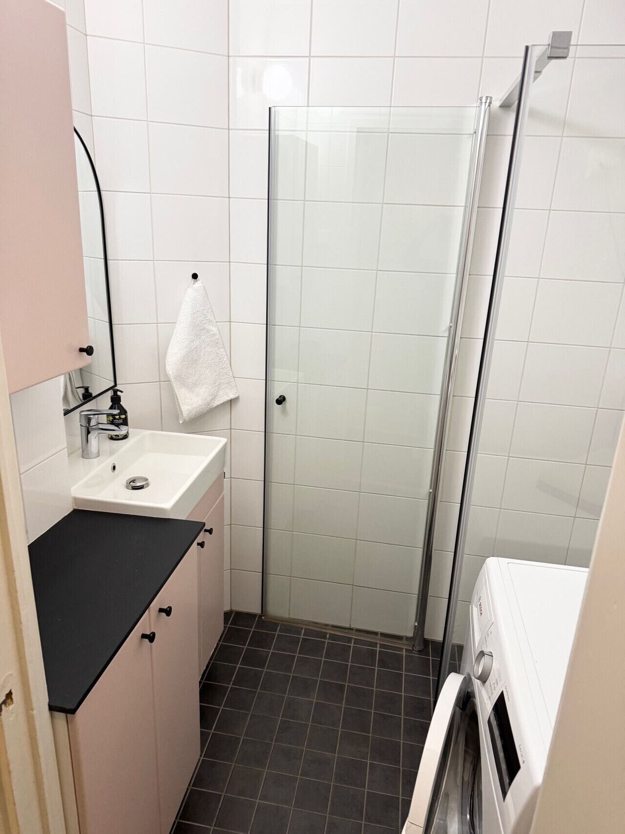 Un baño con lavamanos, cabina de ducha de vidrio y lavadora.