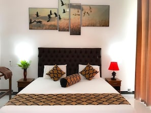 A hotel room with a large bed, a dark headboard, and a red lamp on the nightstand. - Salubrious Resort (Anuradhapura)