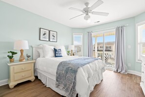 Une chambre à coucher avec un lit, des tables de chevet, un ventilateur de plafond et un balcon avec vue.