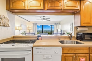 A kitchen with wooden cabinets, a stove, a dishwasher, a microwave, and a view of the balcony. - Direct Oceanfront Condo W/ Private Balcony & BBQ Grills (Cocoa Beach)
