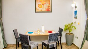 Un comedor con una mesa, cuatro sillas, una planta en maceta, una obra de arte enmarcada y una lámpara fijada a la pared.