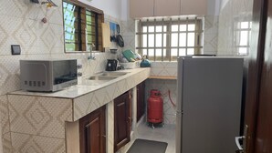 Una cocina equipada con microondas, lavamanos, estufa y un cilindro de gas rojo.