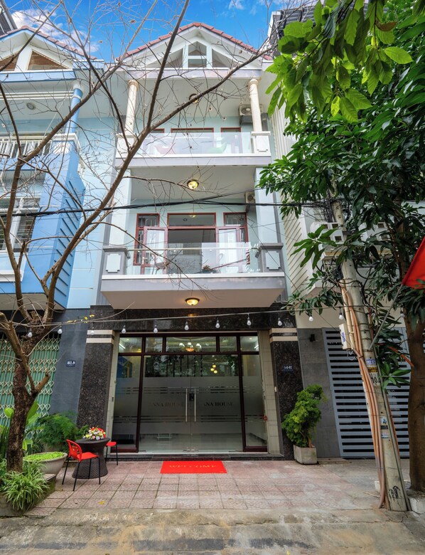 A two-story building with a balcony, a red carpet at the entrance, and outdoor seating with a red chair and table. - Charming 4-bedroom house with AC and WiFi in enchanting Đà Nẵng (Đà Nẵng)