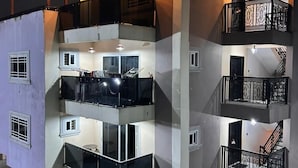 A multi-story building with balconies, a car parked in front, and a staircase leading to the upper floors. - T-Roys Apartments (Accra)