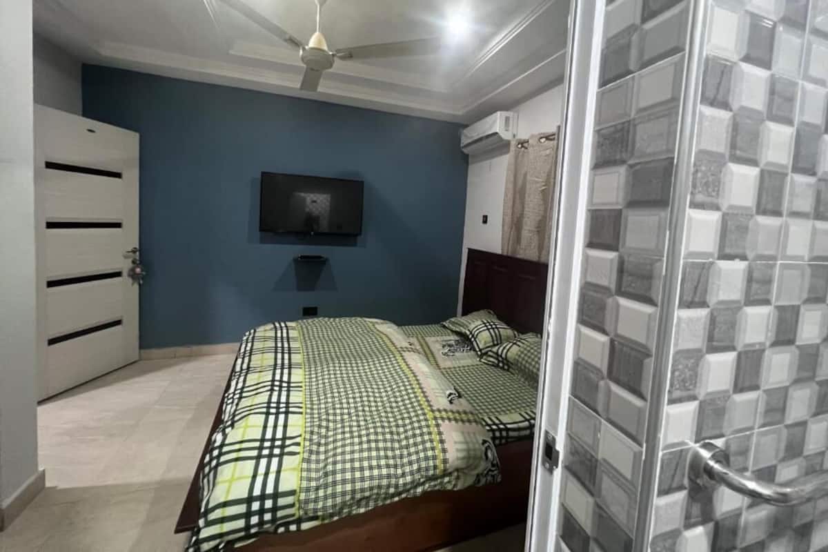 Une chambre à coucher comprenant un lit, un ventilateur de plafond, un téléviseur et un espace douche.