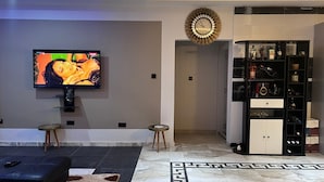 A modern living room with a flat-screen TV, a black sofa, a patterned rug, and a decorative clock. - T-Roys Apartments (Accra)