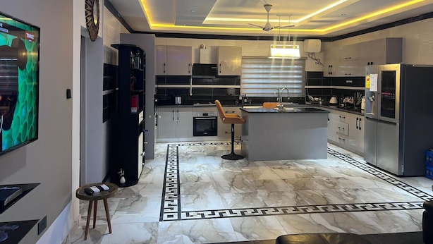 A modern kitchen with a central island, built-in appliances, and a marble floor. - T-Roys Apartments (Accra)