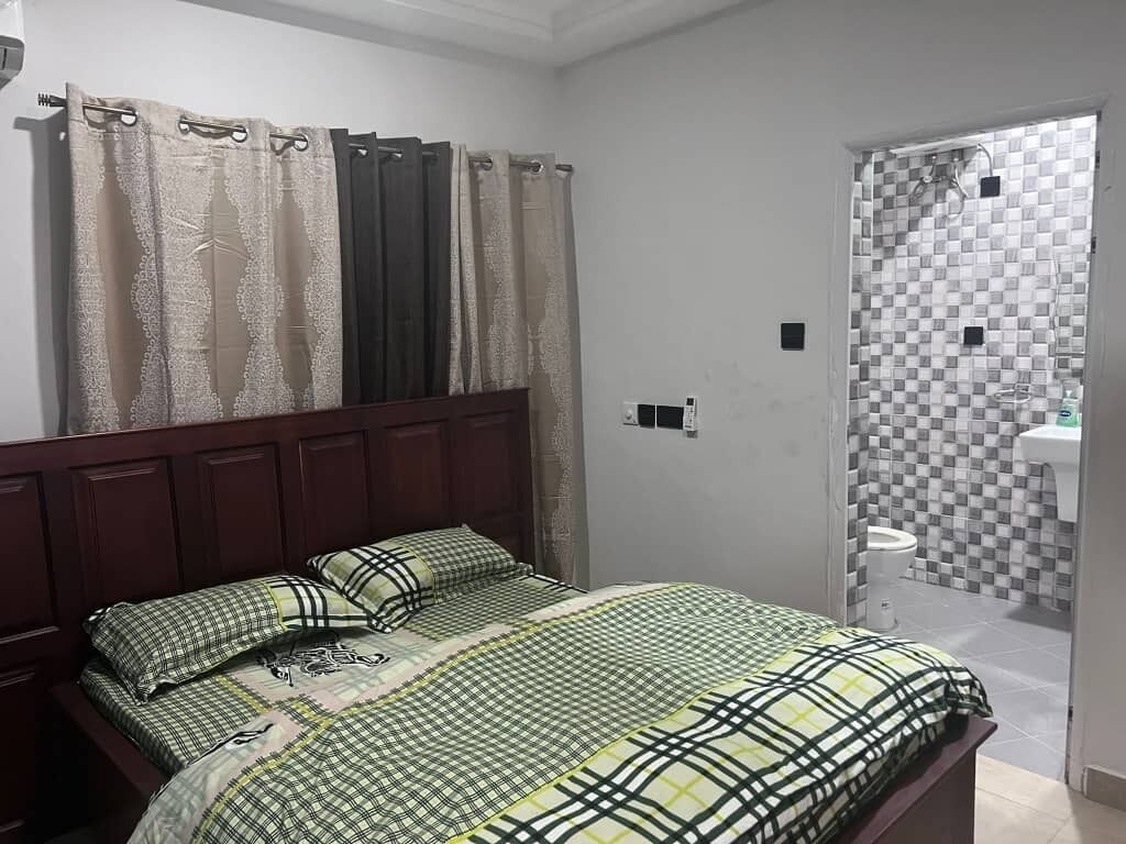 A bedroom with a bed, curtains, and a bathroom visible through an open door.