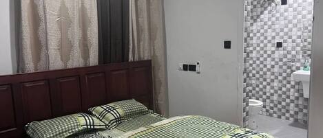 A bedroom with a bed, curtains, and a bathroom visible through an open door.