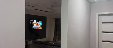 A room with a flat-screen TV mounted on the wall, a ceiling fan, and a sliding door.