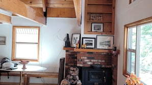 A cozy cabin interior with a brick fireplace, wooden beams, and a dining area with a table and bench. - Charming 2-bdrm cabin in Fawnskin, with Wifi & just a 5 minute walk to the lake (Fawnskin)