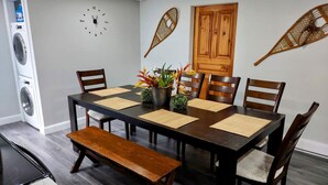 Un comedor con una mesa larga, sillas de madera, un banco y un reloj en la pared.