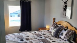 A bedroom with a bed, a nightstand, a wall-mounted lamp, a window with a curtain, and a ceiling fan. - Panache Royale 2.... (Québec City)