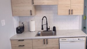 A compact kitchen with wooden cabinets, a stainless steel sink, a dishwasher, and a white tiled backsplash. - Panache Royale 2.... (Québec City)