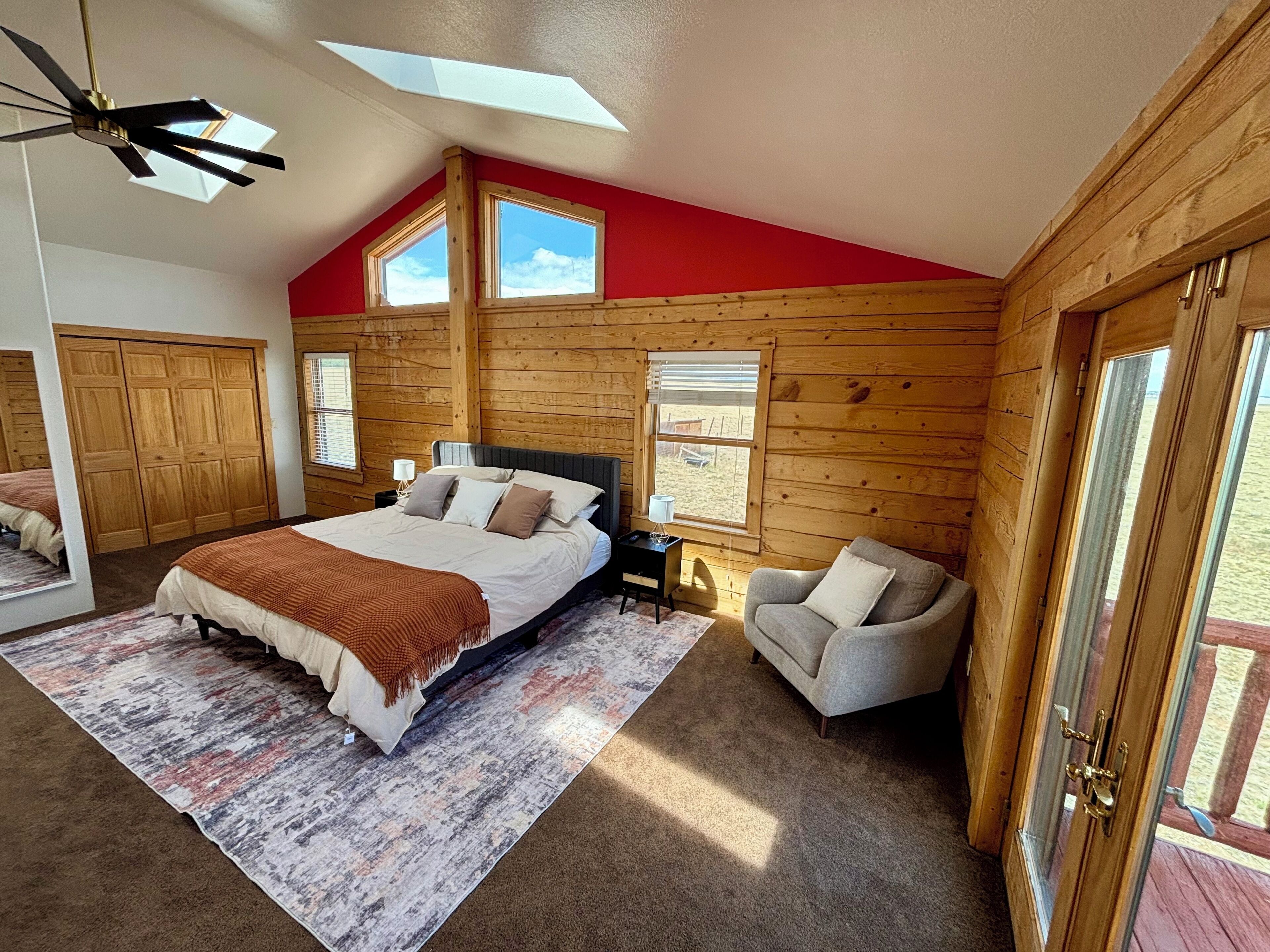Un dormitorio con cama, mesita de noche, silla y un ventanal grande.