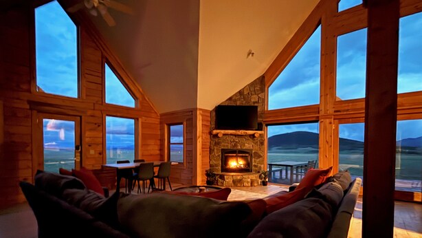 Una sala de estar acogedora con chimenea de piedra, mobiliario de madera y grandes ventanales que ofrecen vistas al exterior.