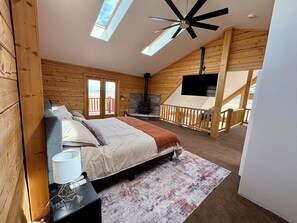 Ein gemütliches Schlafzimmer mit Bett, Fernseher, Kamin und einem Balkon mit Holzgeländer.
