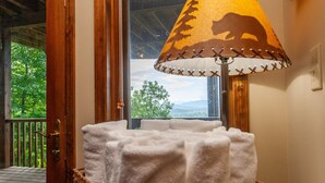 Una habitación acogedora con ventana que da a un paisaje pintoresco, una lámpara con pantalla en forma de oso y una cesta con toallas dobladas.