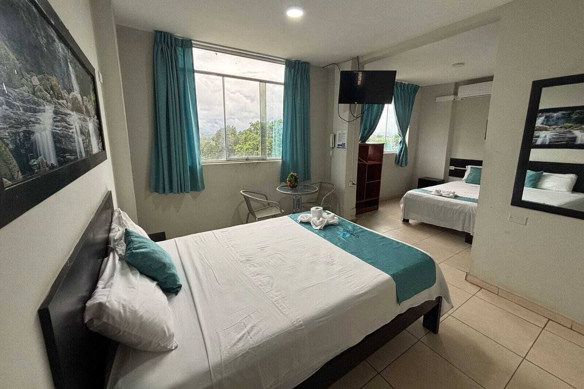 Une chambre d’hôtel avec un lit, un bureau, une chaise, une télévision et une fenêtre avec des rideaux.