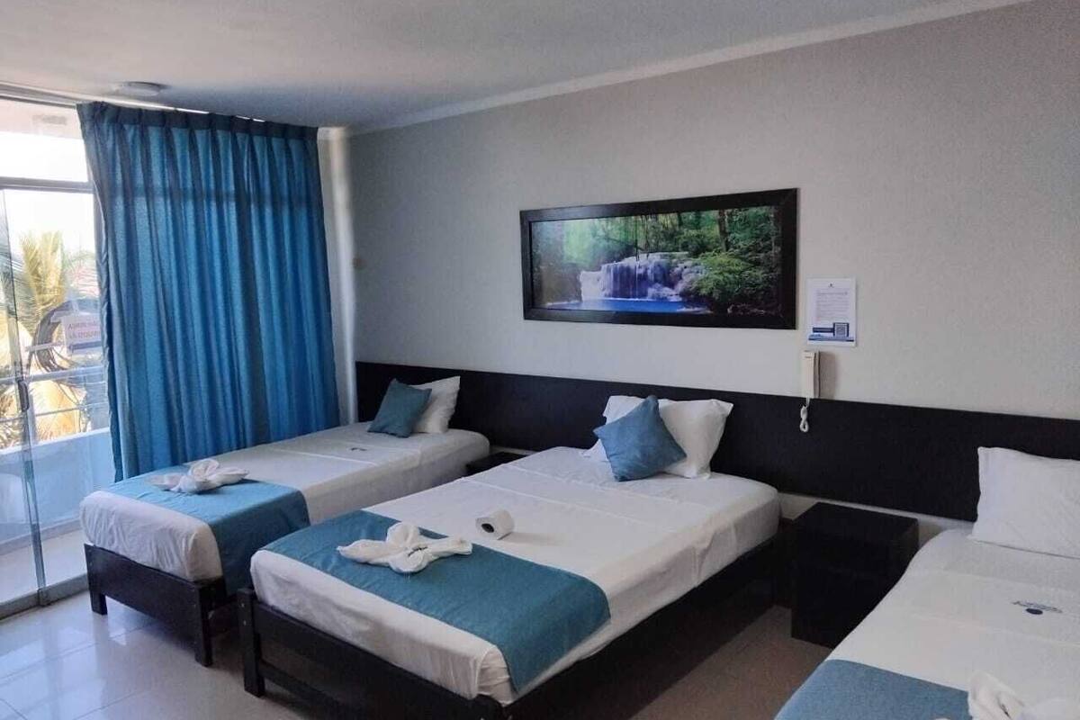 Une chambre d’hôtel avec deux lits simples, un téléviseur fixé au mur et une fenêtre avec des rideaux bleus.