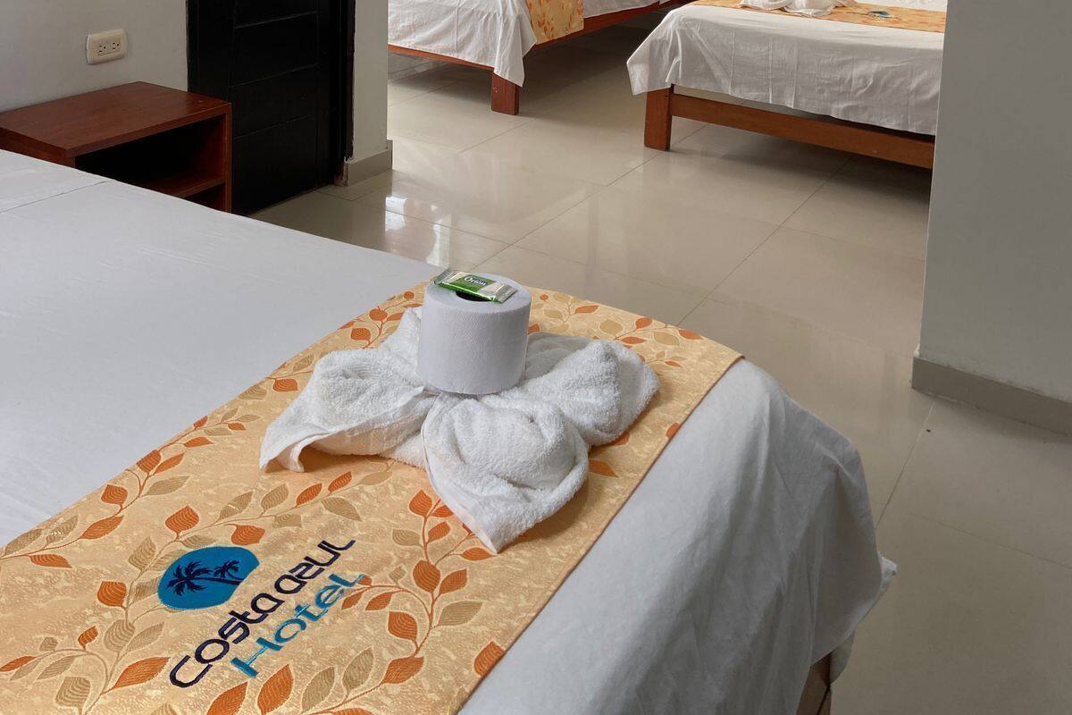 Une chambre d’hôtel avec deux lits simples, une grande fenêtre avec des rideaux orange, un climatiseur fixé au mur et un tableau encadré représentant un château.